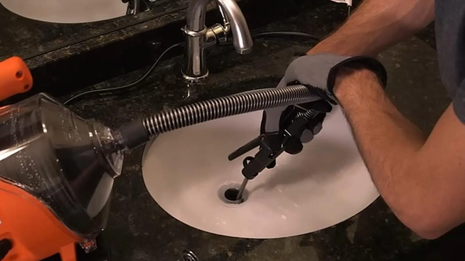 Hand-cranked drain snake being fed into a kitchen sink drain