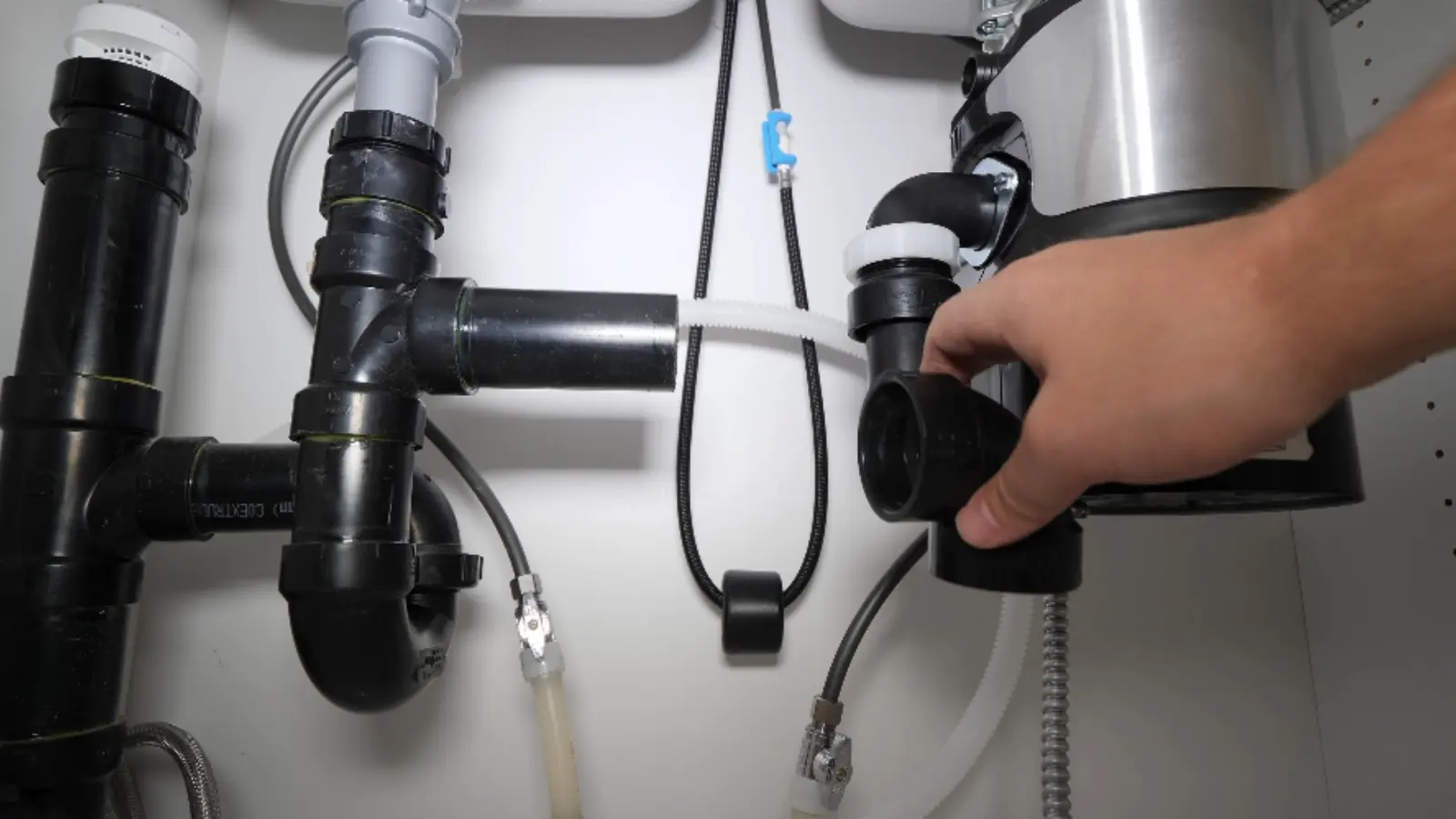 Hand reaching up to a garbage disposal under a kitchen sink